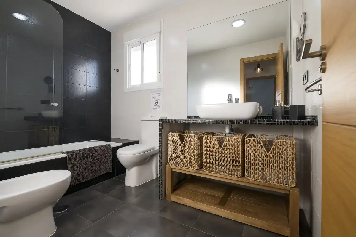 A modern bathroom with a bathtub, toilet, and sink beneath a large mirror.