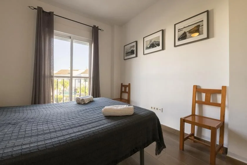 A bedroom with a bed, two wooden chairs, and framed pictures on the wall.