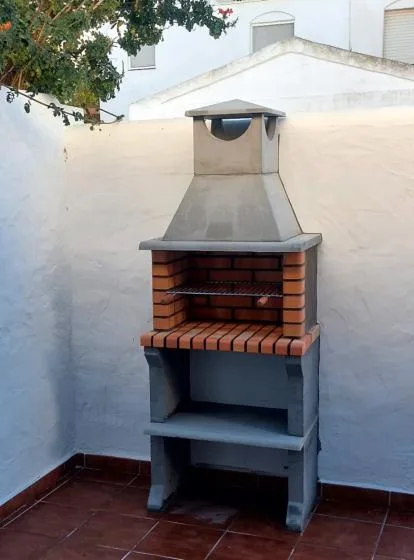 An outdoor brick barbecue stands against a white wall on a tiled patio.