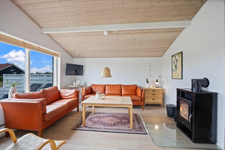 A bright living room with orange seating, a wooden coffee table, and a black stove.