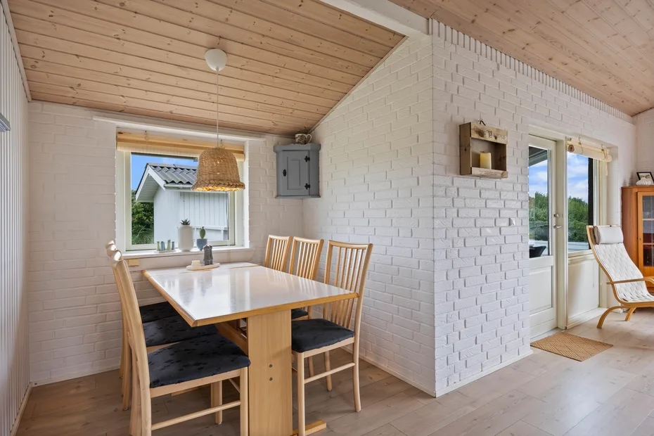 A dining area with a wooden table beside large windows and a white brick wall.