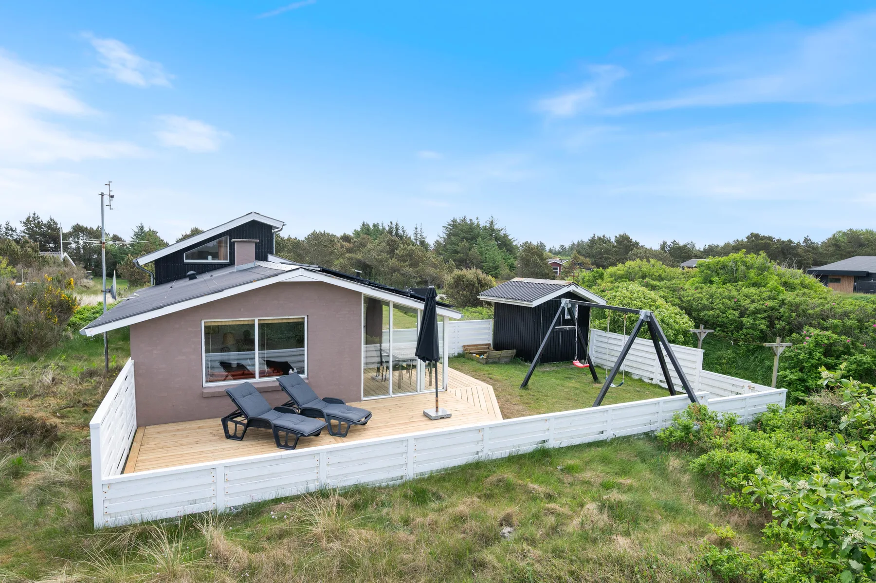 A vacation house with a fenced deck, outdoor loungers, and a swing set.