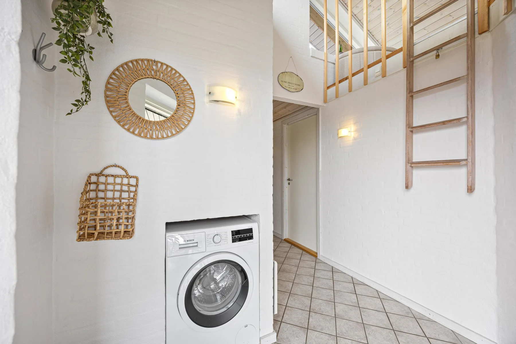 A bright hallway with a washing machine, wall mirror, and ladder to an upper level.