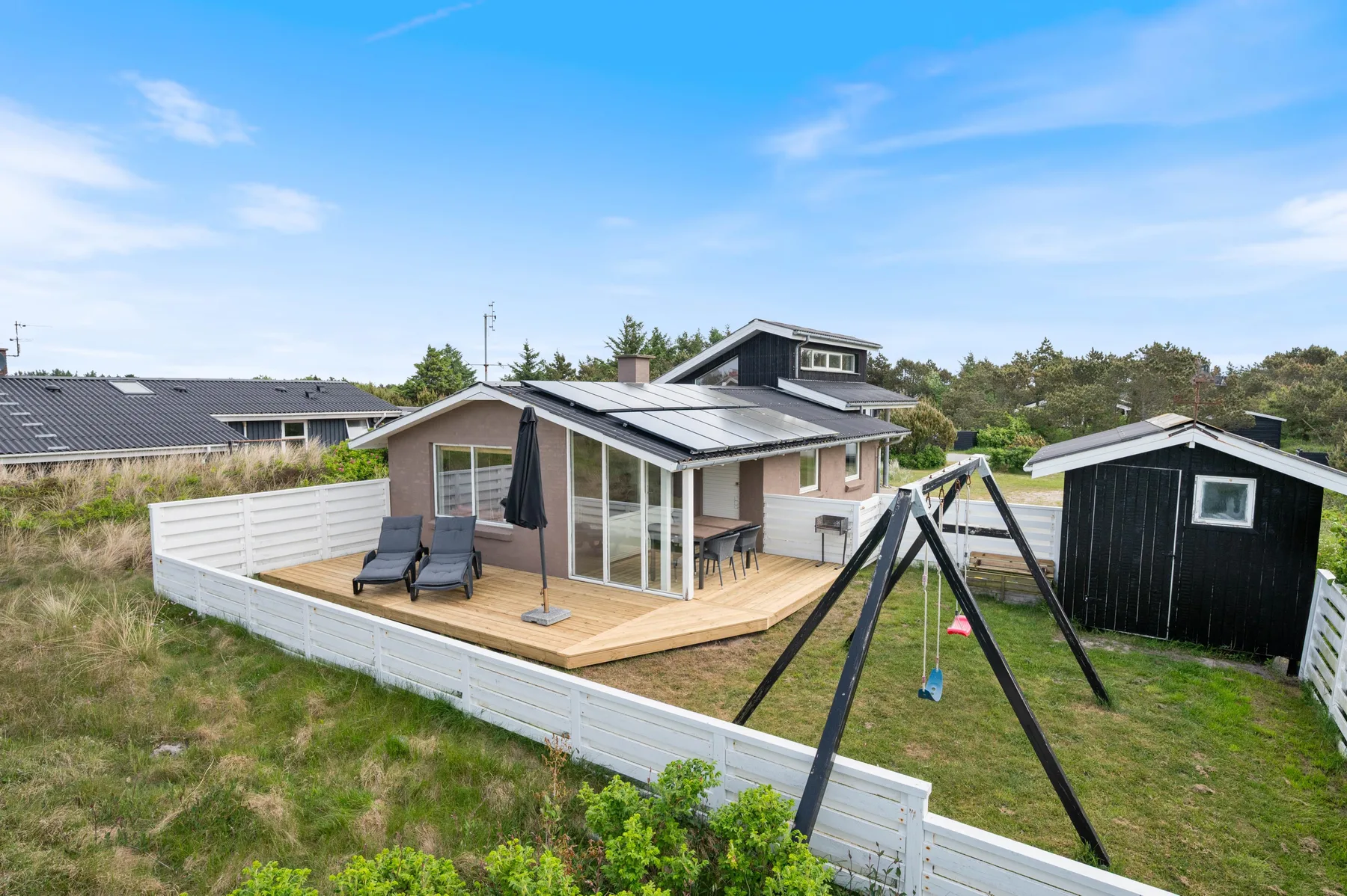 A holiday house with a wooden deck and an outdoor swing in the yard.