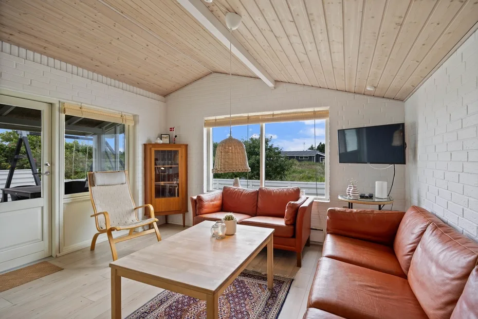 A living room with leather seating, a coffee table, and windows overlooking greenery.