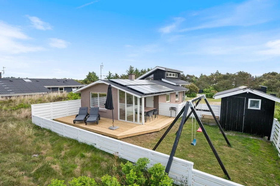 A modern house opens onto a wooden deck with outdoor seating and a swing set.