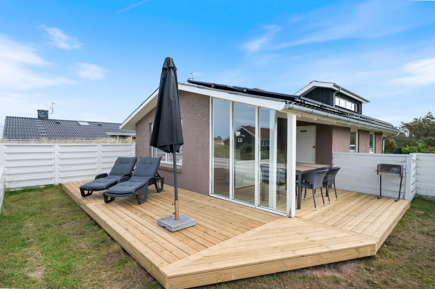 A house exterior with a wooden deck, outdoor seating, and glass doors.