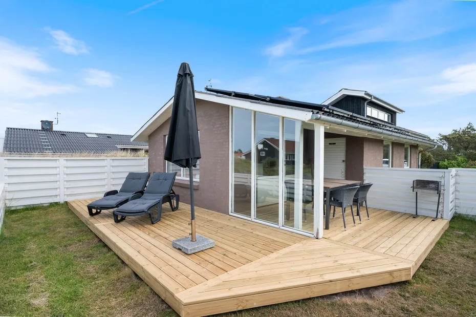 A house patio with a wooden deck, outdoor seating, and a closed umbrella.