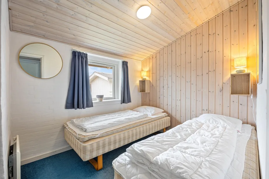 A bedroom with two single beds, a window, and light wood-paneled walls.