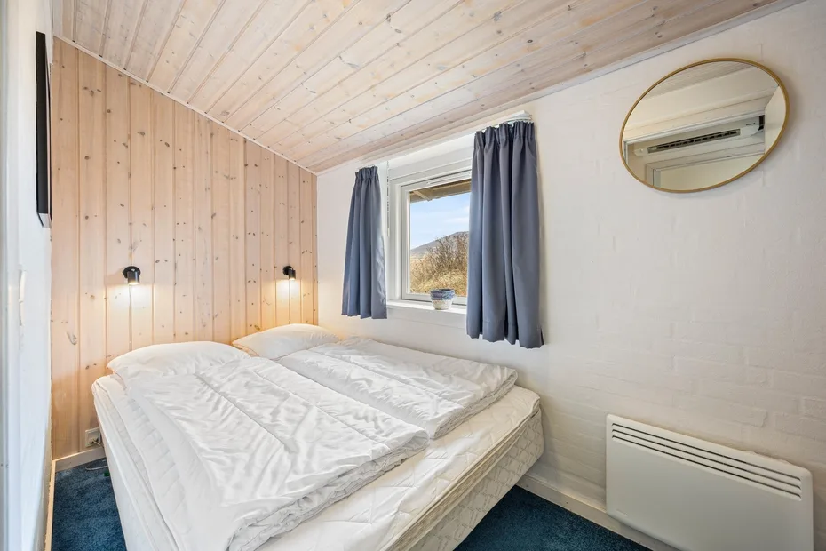 A bedroom with a bed beneath a window framed by dark curtains.