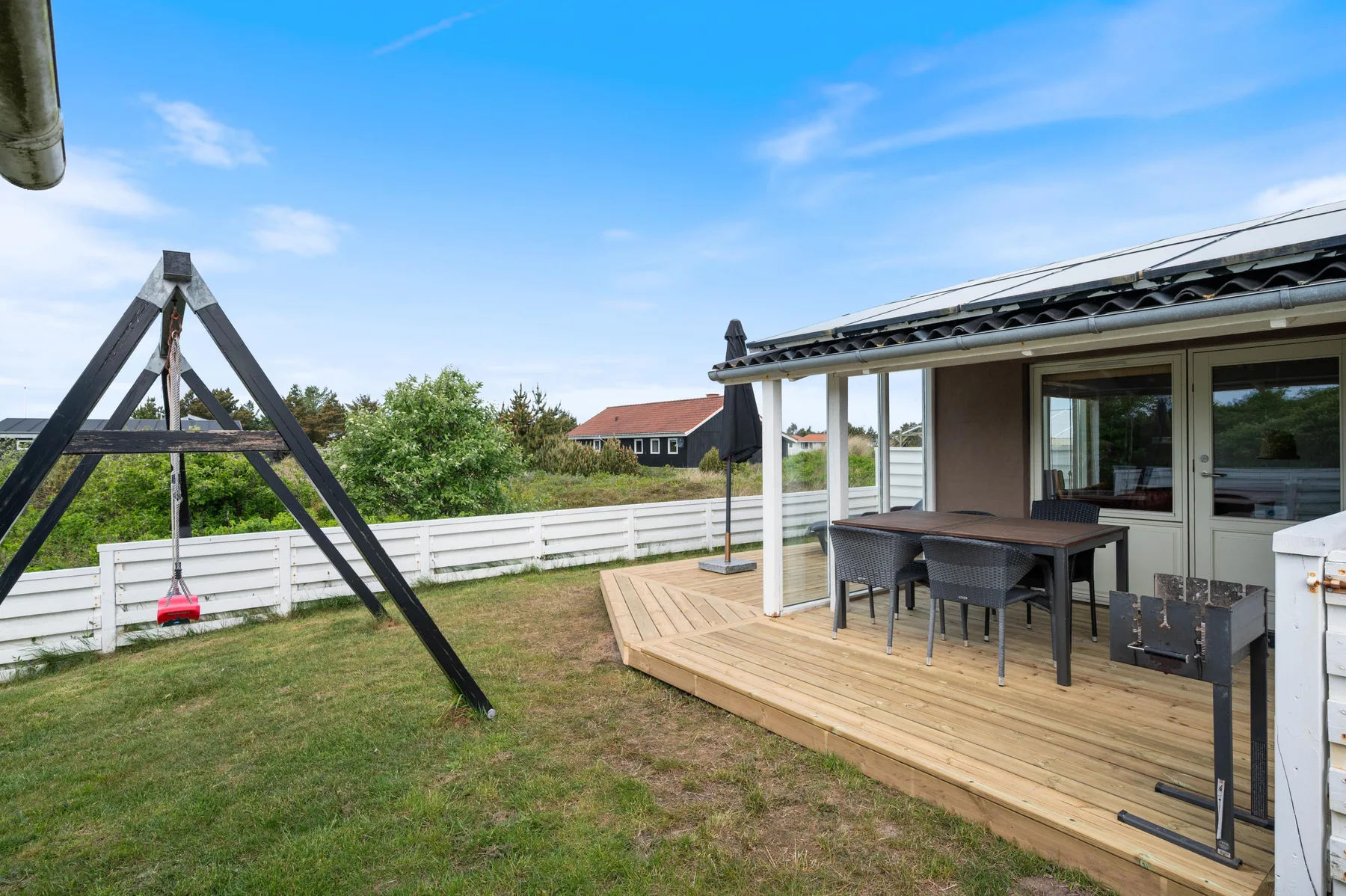A wooden deck with outdoor seating overlooks a grassy yard with a swing frame.
