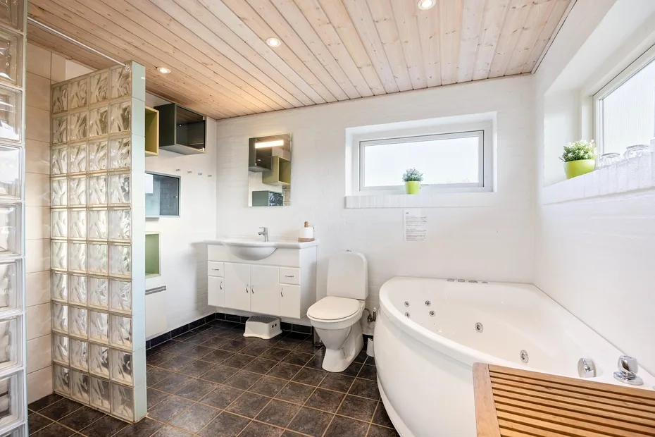 A bright bathroom with a bathtub, toilet, and vanity beneath a wood-paneled ceiling.