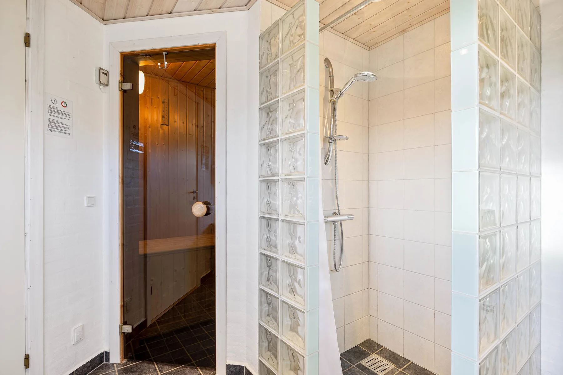 A tiled bathroom with a glass-block shower area and a wooden sauna.