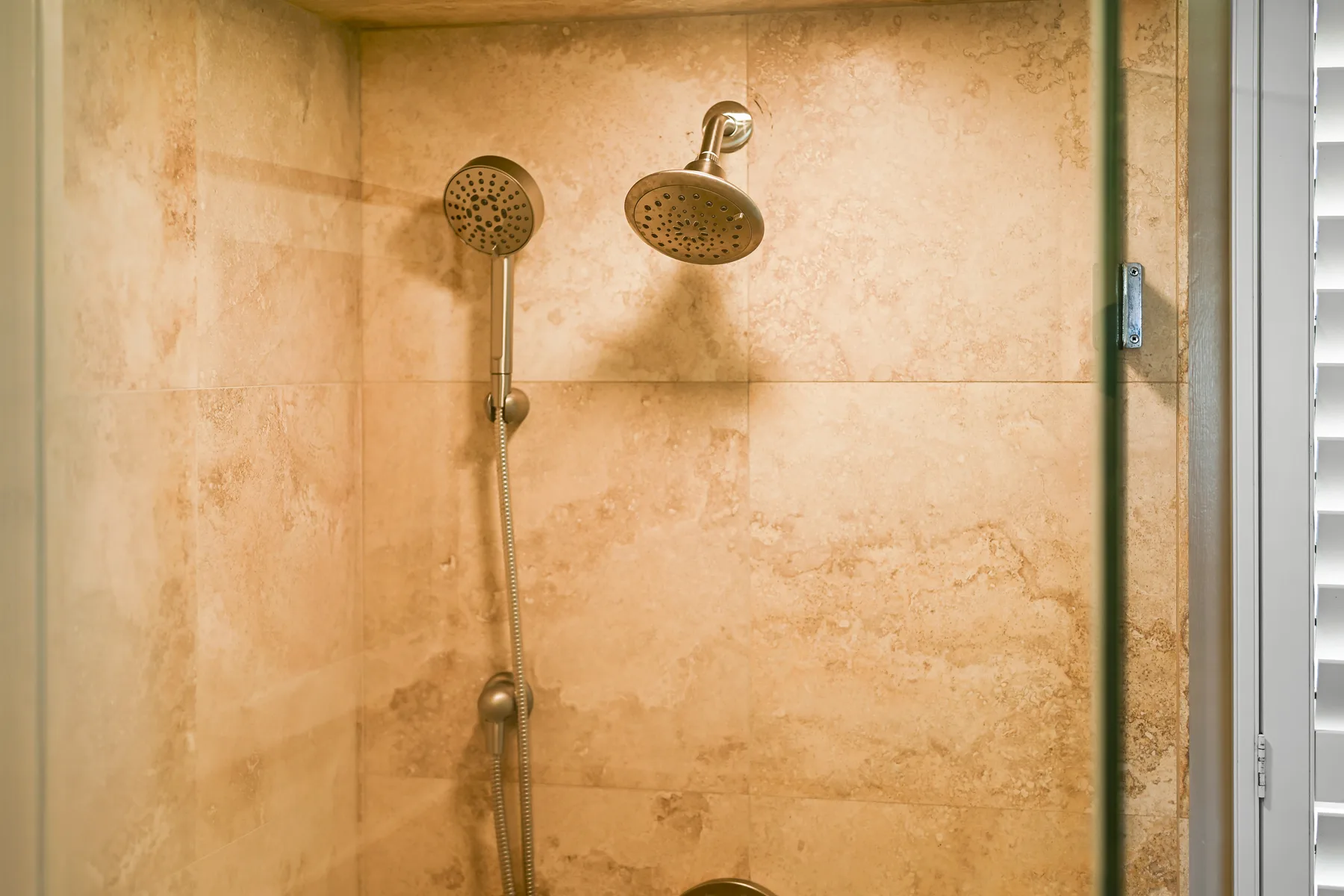 Una ducha revestida de azulejos con dos cabezales y una ducha de mano.