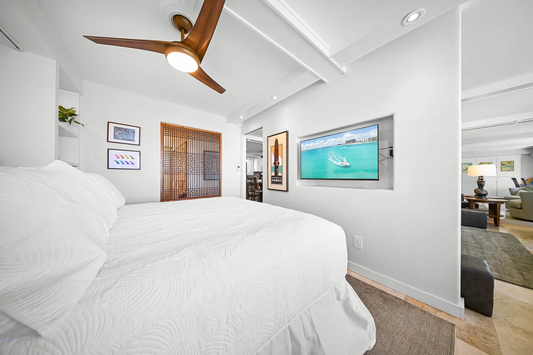 Un dormitorio luminoso con ropa de cama blanca y un televisor en la pared.