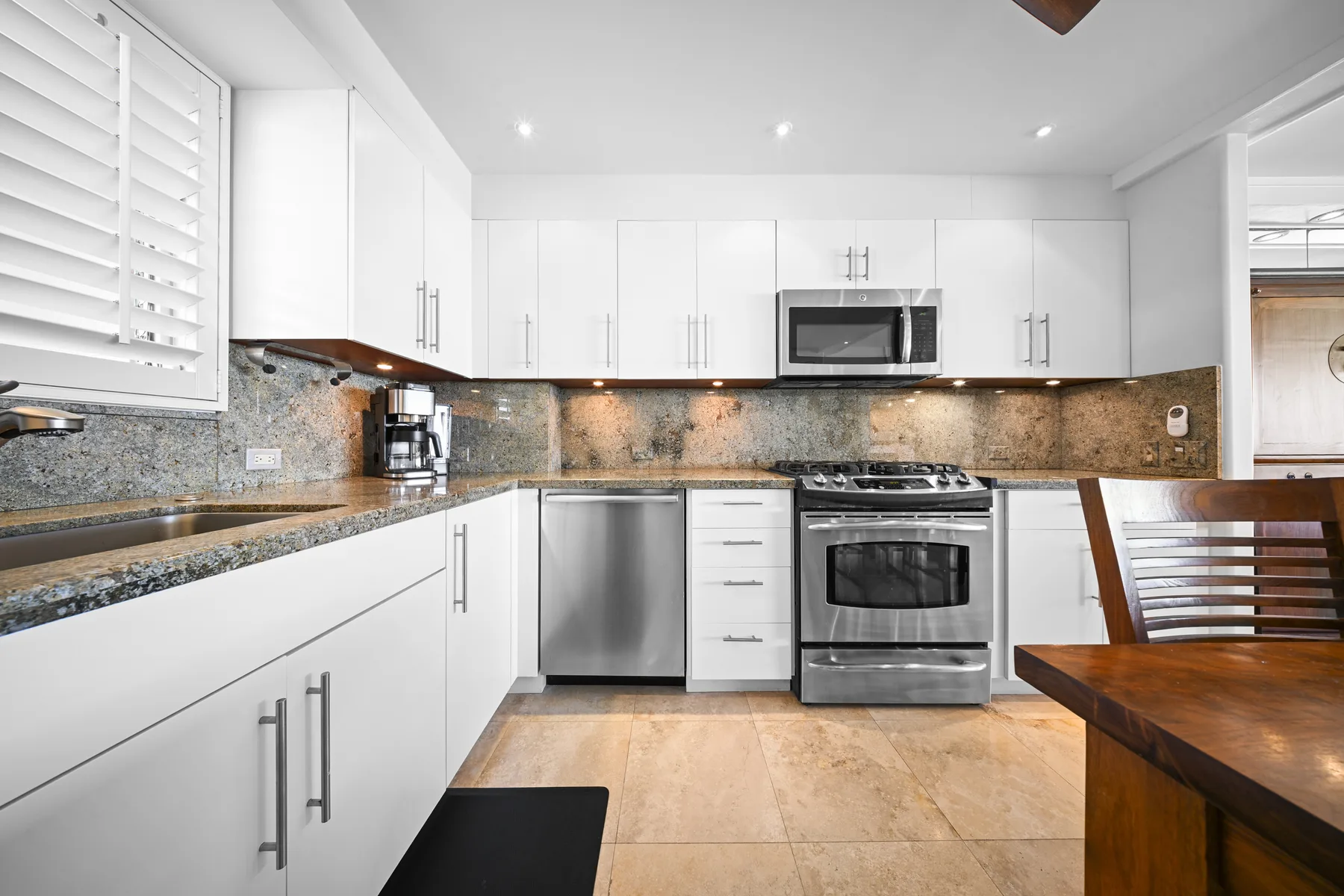 Una cocina luminosa con gabinetes blancos, encimeras de piedra y electrodomésticos de acero inoxidable.