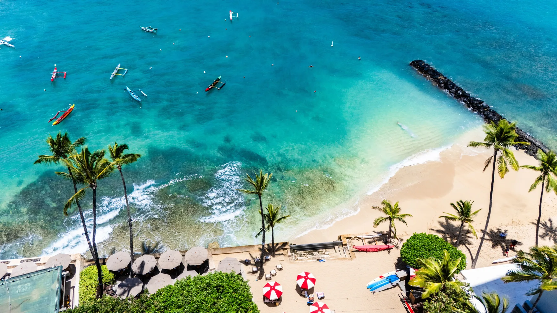 Vista aérea de una playa tropical con palmeras y embarcaciones en aguas turquesas.