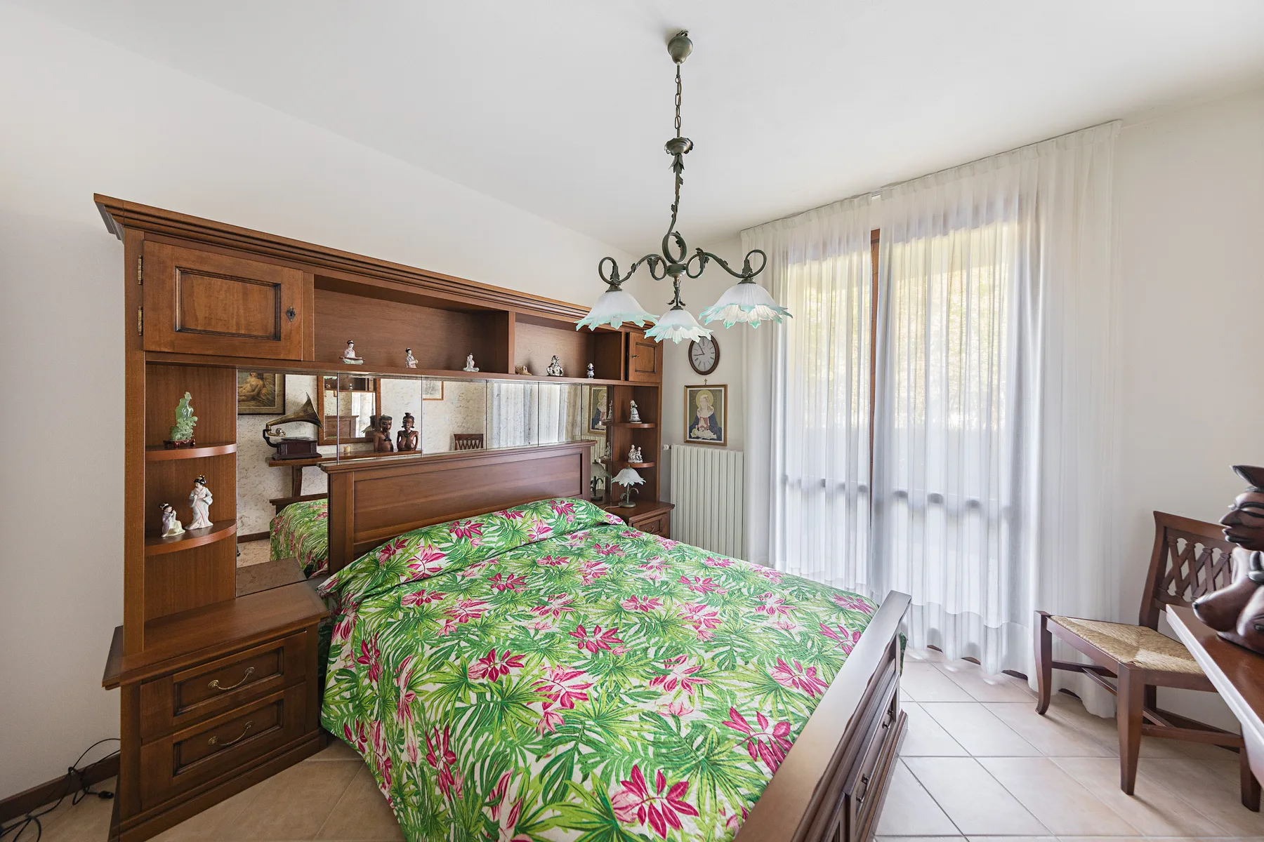 A bedroom with a wooden bed covered in a bright floral bedspread.