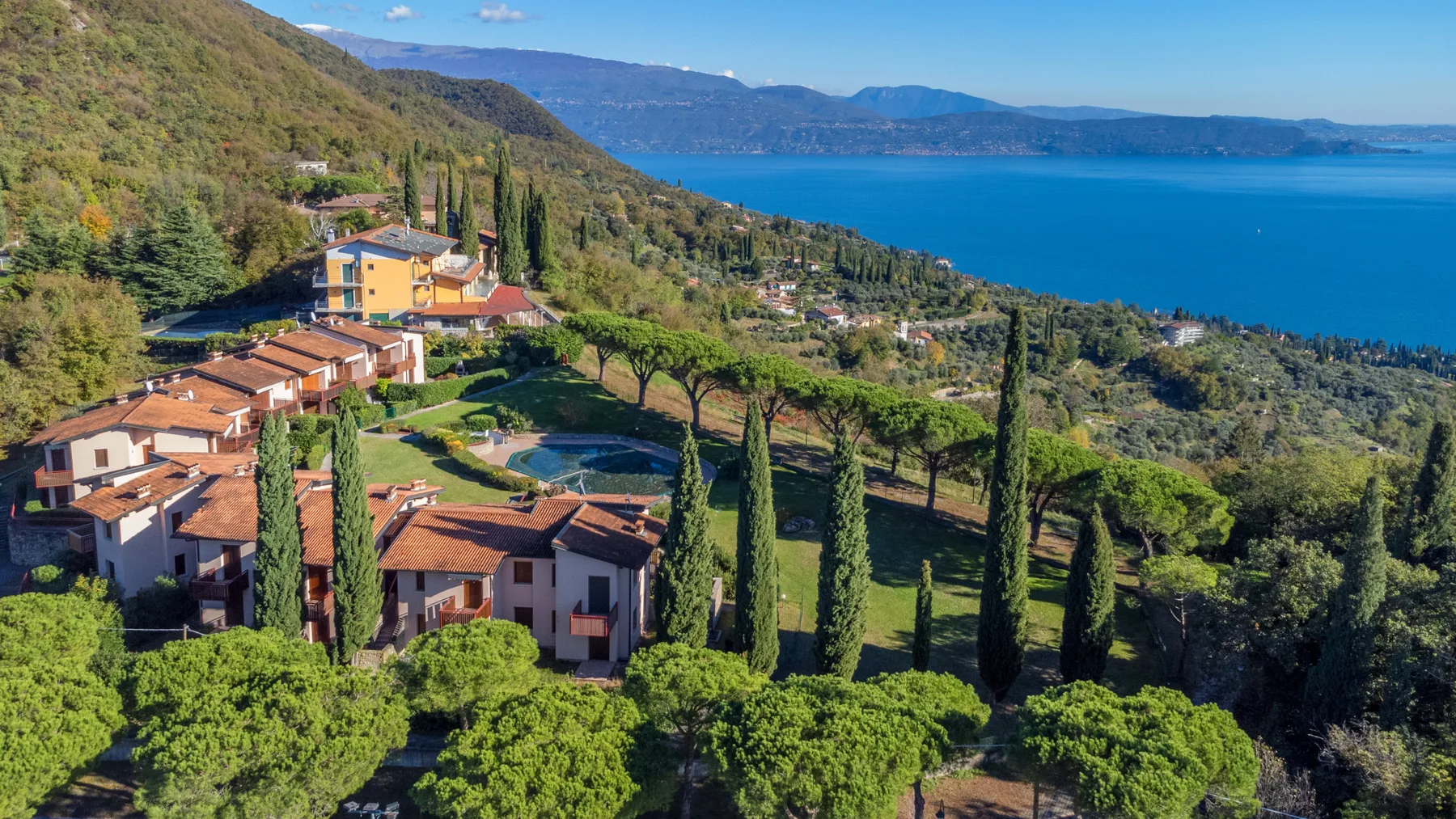 A hillside residential complex overlooks a blue lake and surrounding greenery.