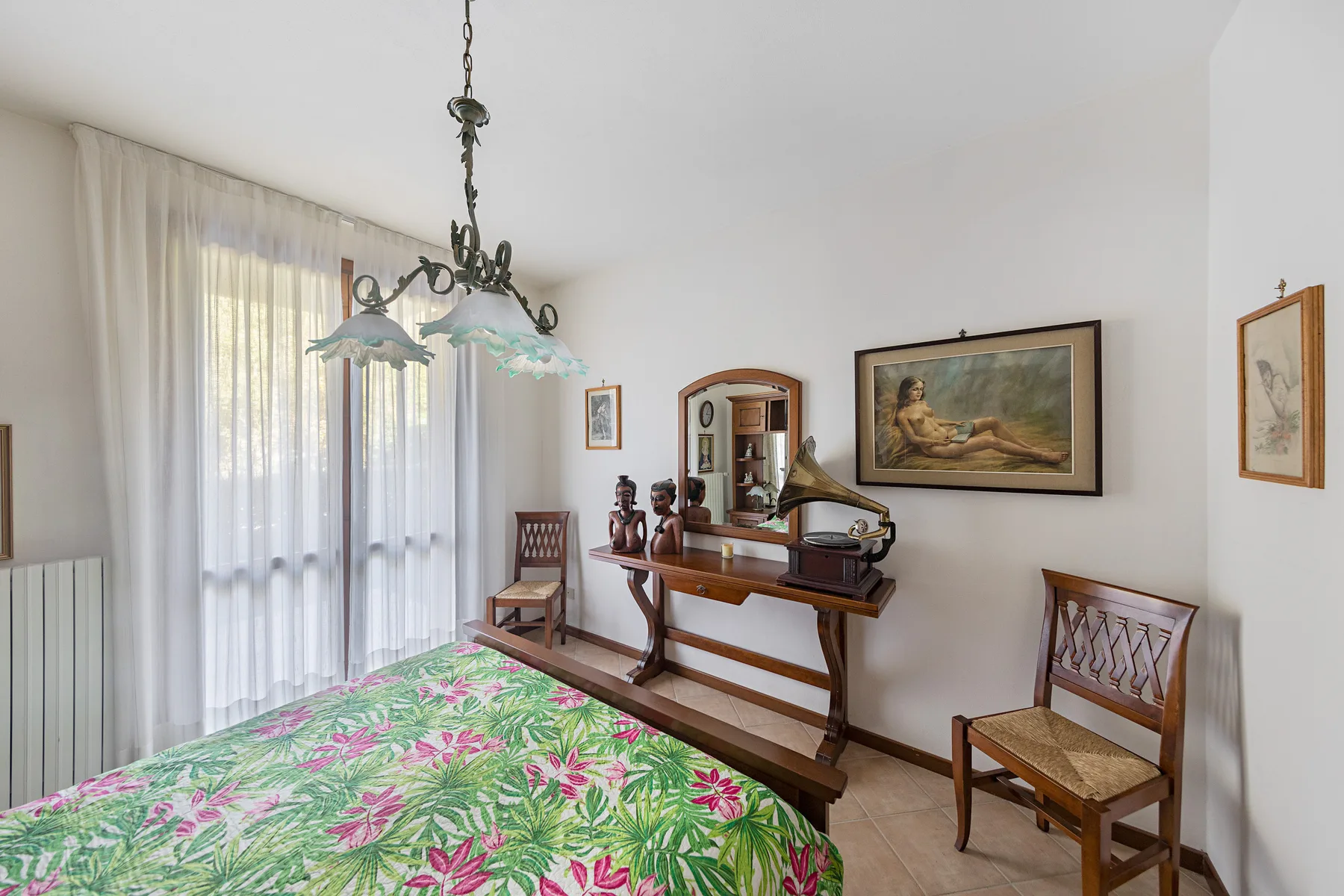 A bedroom with a floral bedspread, wooden chairs, and a gramophone.