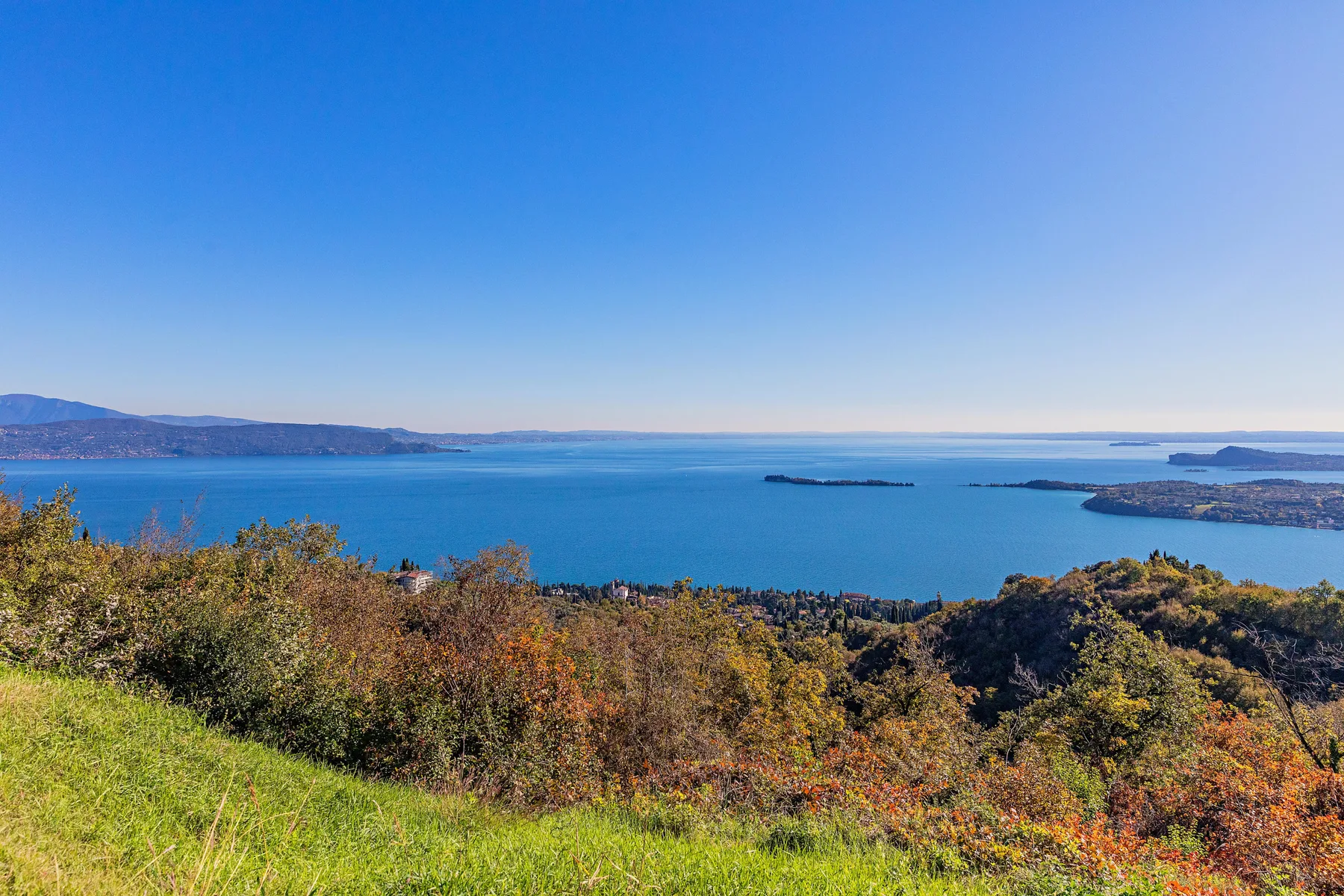A wide blue lake stretches beyond a hillside covered with autumn-colored trees.