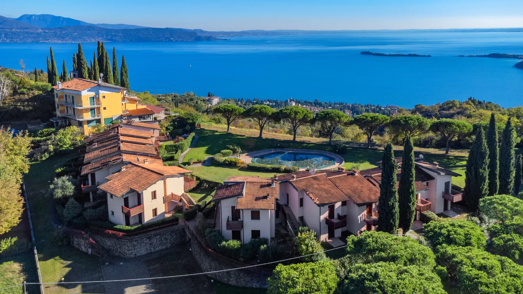 A lakeside property with terracotta-roofed buildings, landscaped grounds, and a swimming pool.