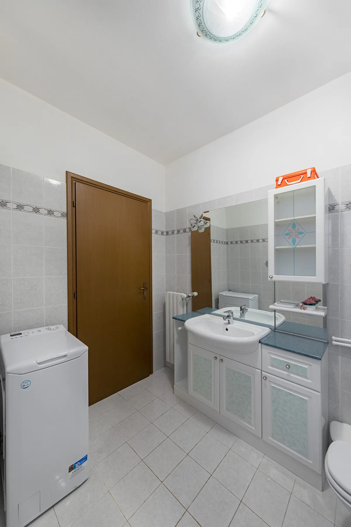 A bathroom with a sink vanity, wall cabinet, and washing machine.