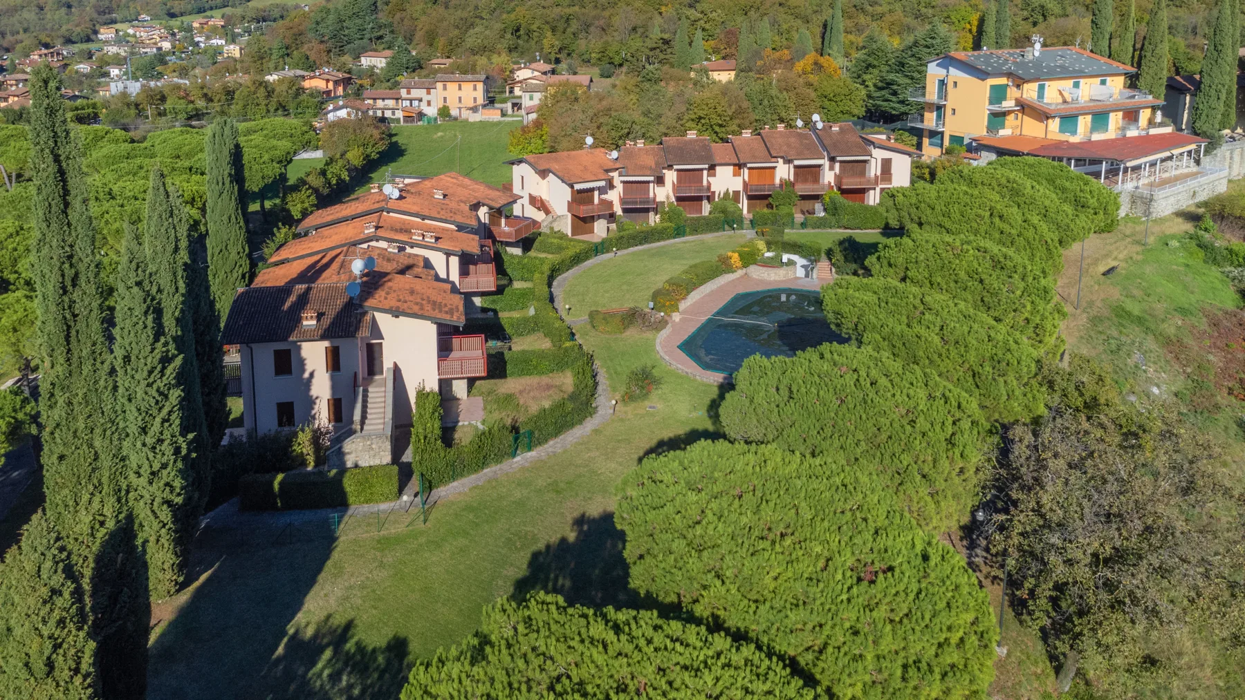 Aerial view of a landscaped residential complex with buildings and a small pool.