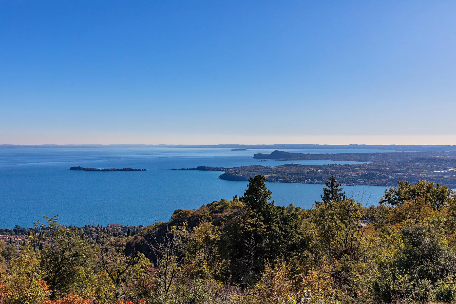 A broad blue bay stretches beyond a wooded hillside beneath a clear sky.