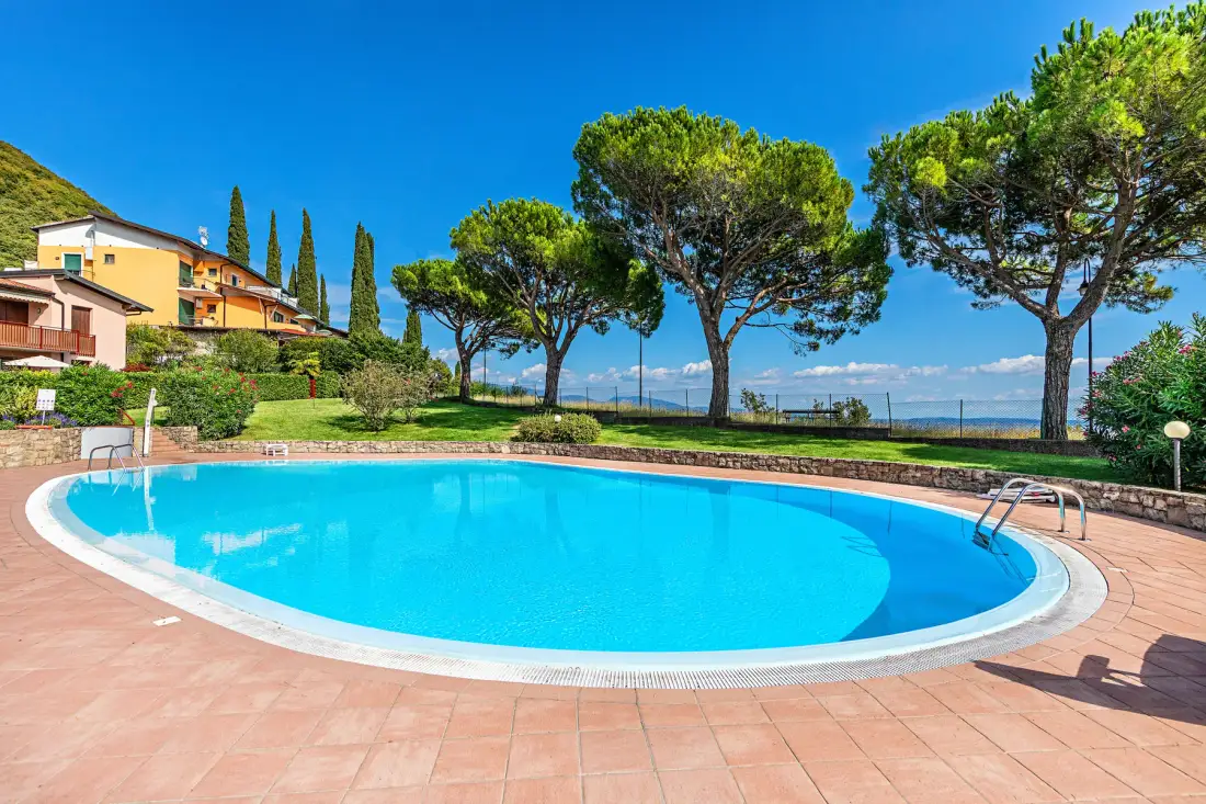 An outdoor swimming pool sits beside a landscaped garden with trees.