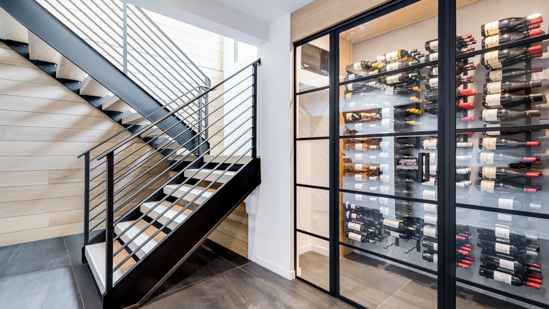 A modern staircase beside a glass-fronted wine storage room.