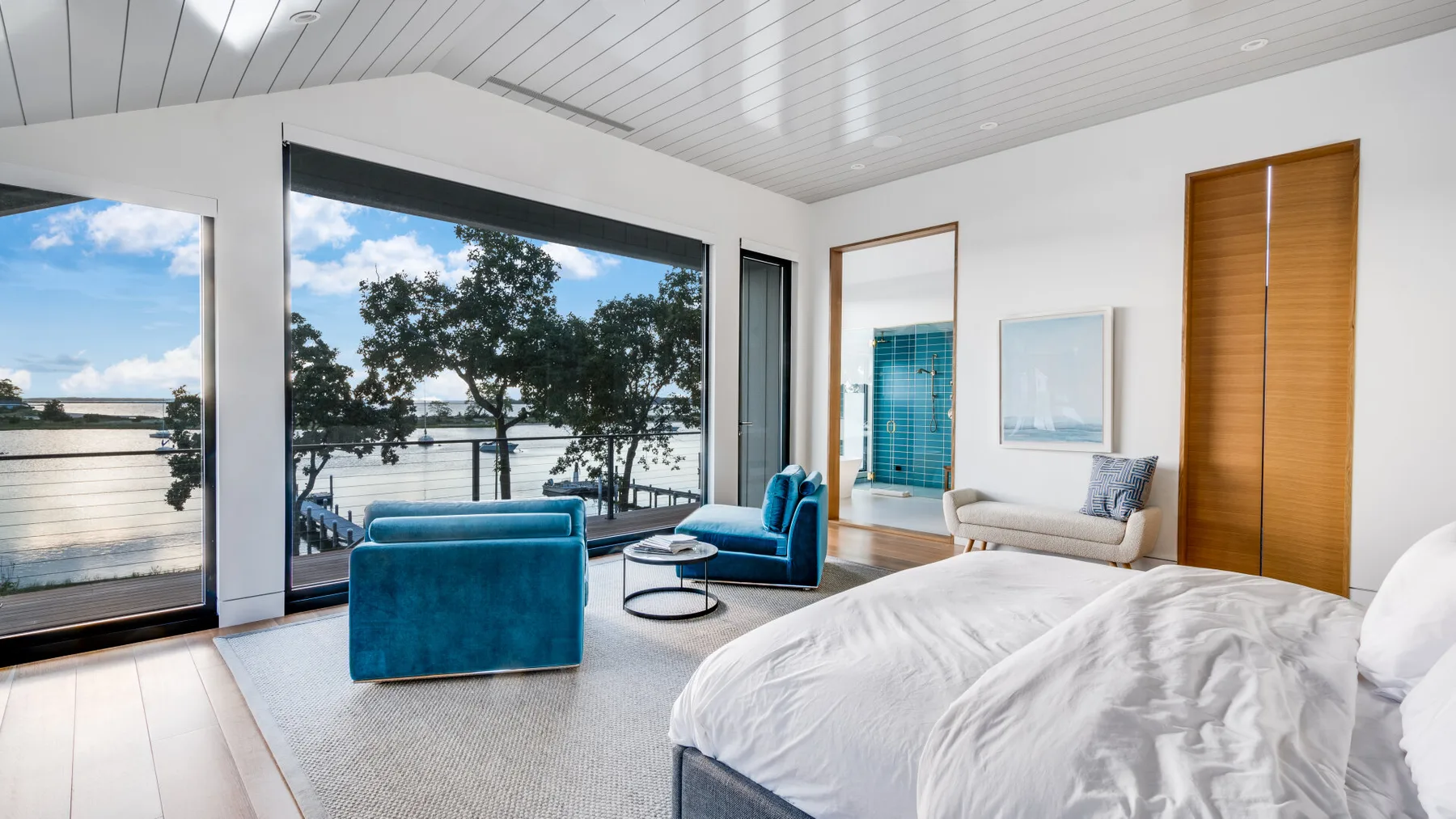 A bright bedroom with a large bed beside windows overlooking the water.