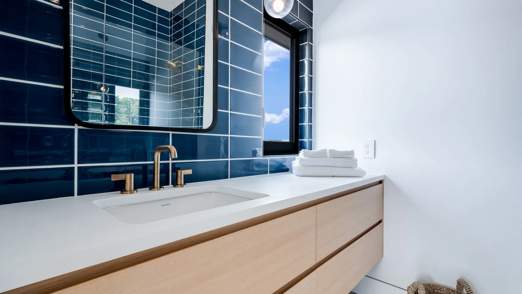 A bathroom vanity with a wide sink, blue tiled wall, and mirror.