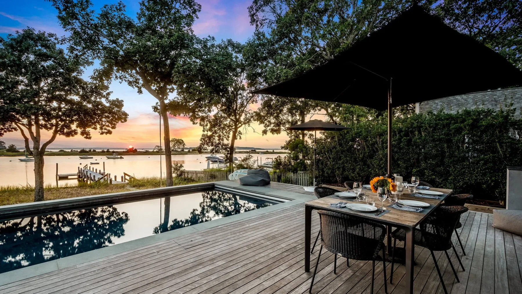 A poolside deck has an outdoor dining table beneath a large umbrella.