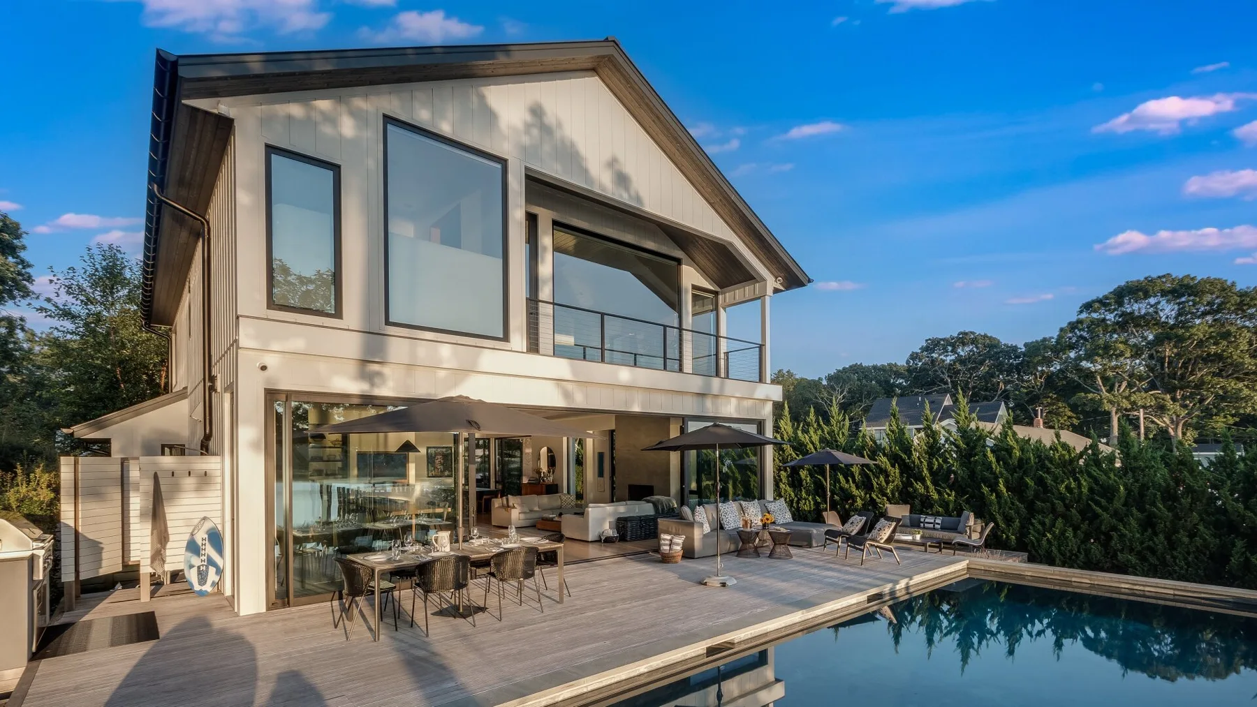 A modern house opens onto a wooden pool deck with outdoor seating.