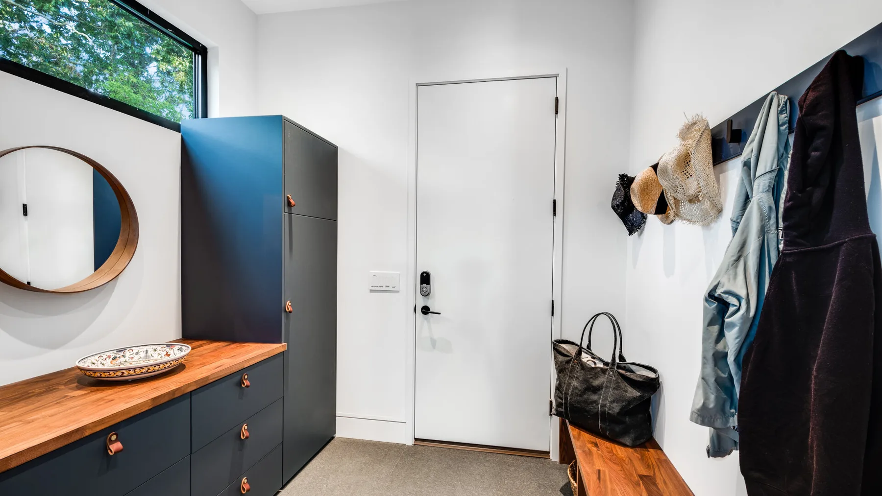 An entryway with a wooden bench, wall hooks, and a round mirror.