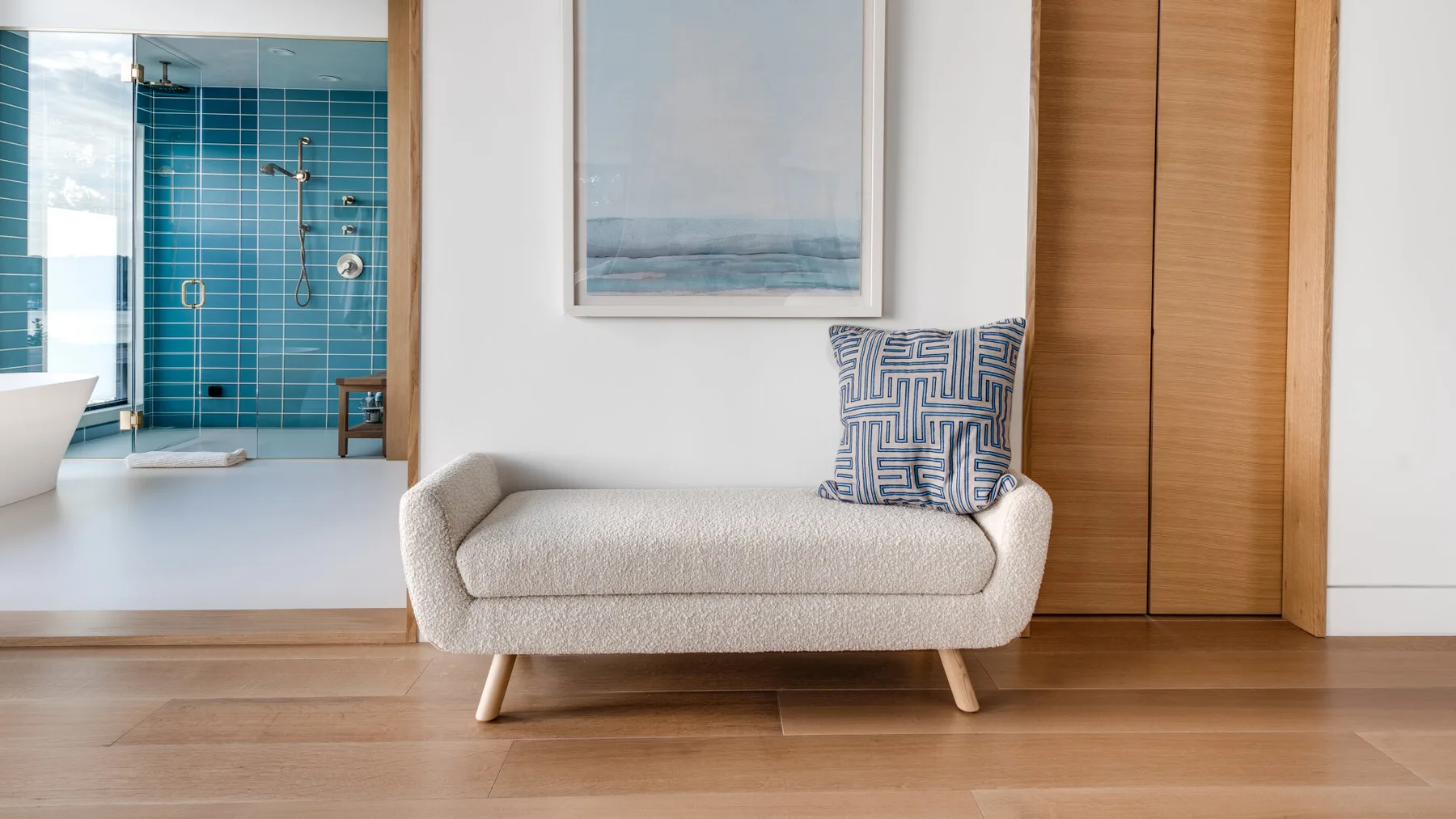 A light-colored seating area sits beside a tiled bathroom, with a framed picture above.
