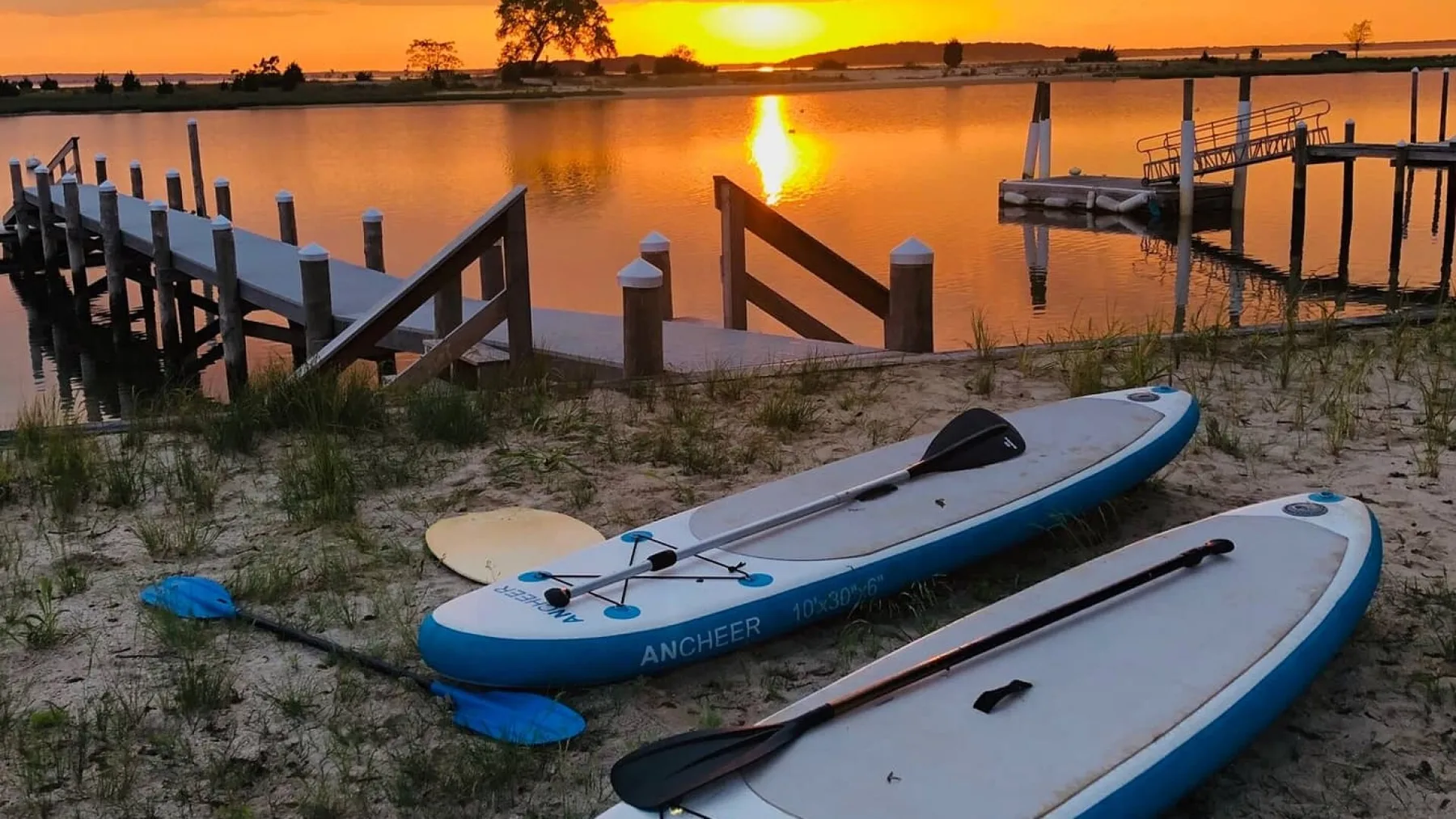Kayaks rest on a sandy shore beside wooden docks at sunset.