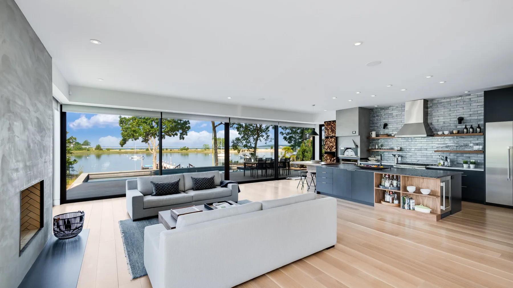 A modern living room opens onto large windows overlooking a lake.