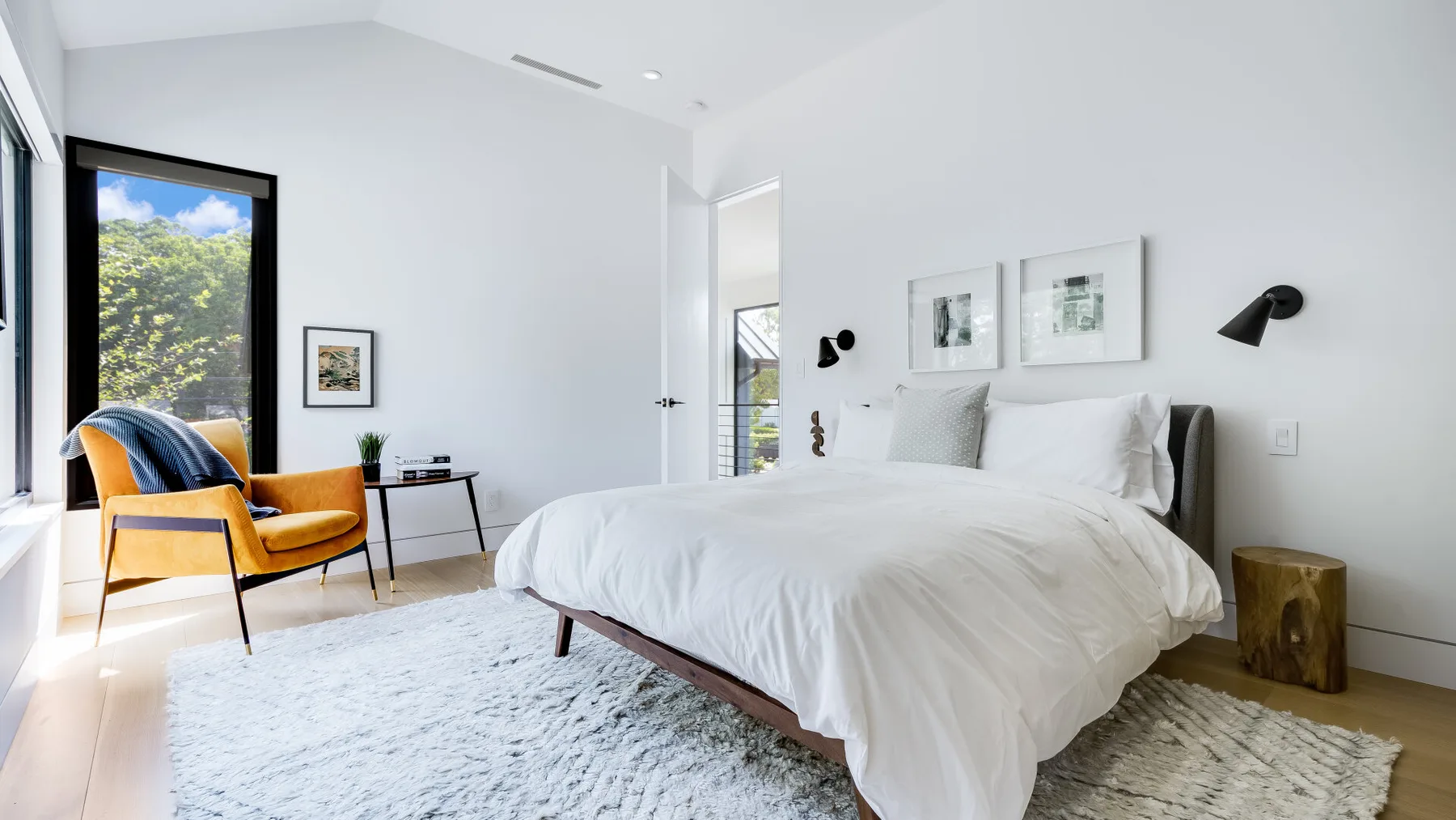 A bright bedroom with a white bed and large windows.