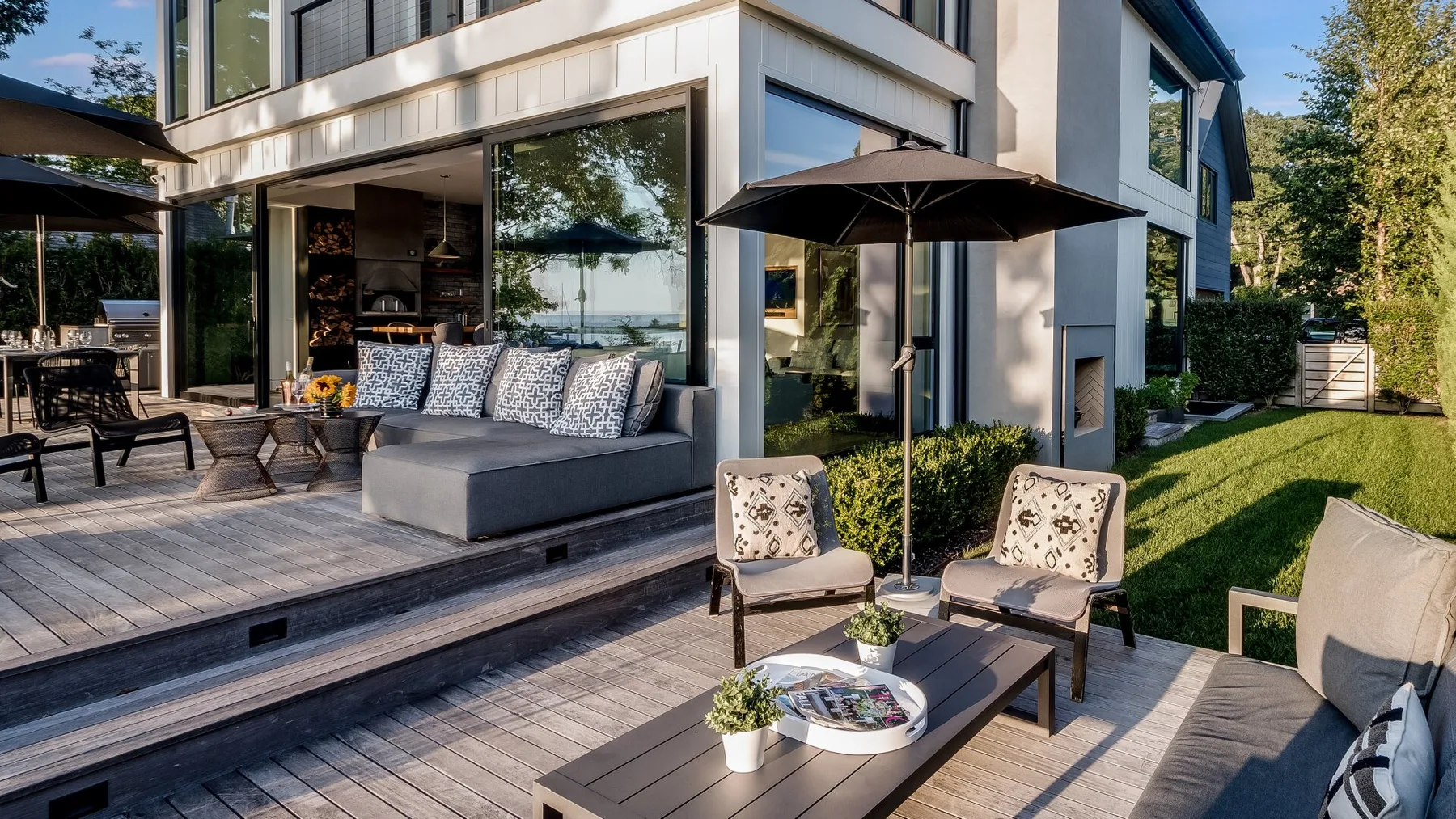 An outdoor patio with seating and a dark umbrella beside a modern house.