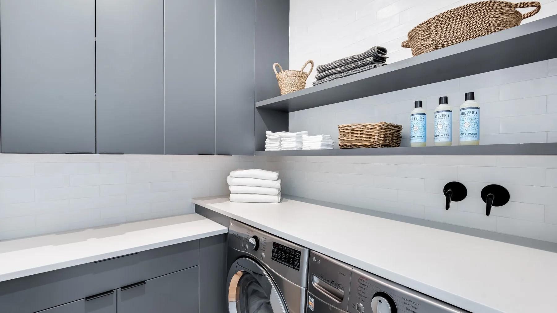 A modern laundry room with a washer and dryer beneath a long countertop.