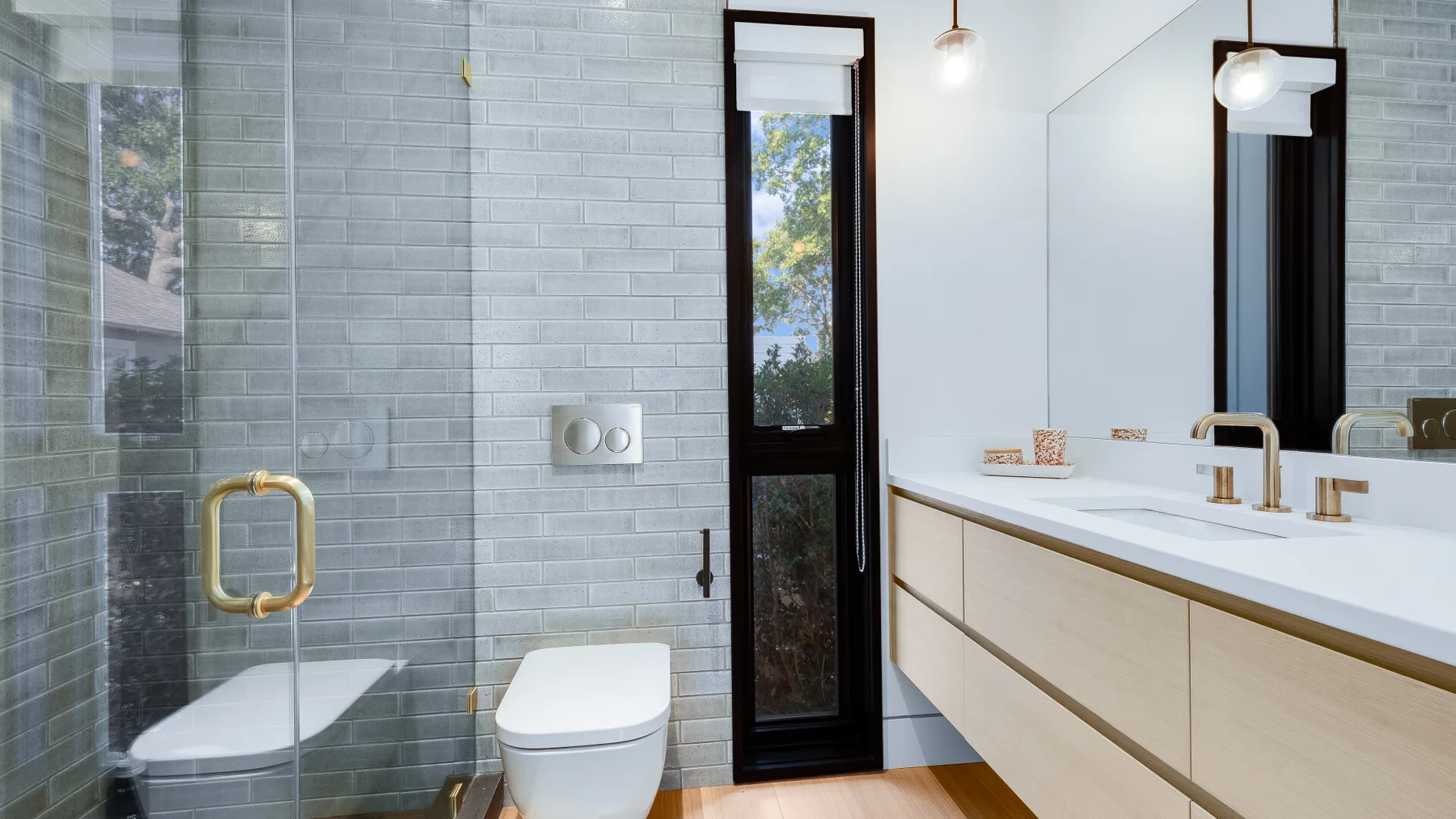 A modern bathroom with a glass shower, toilet, and long vanity.