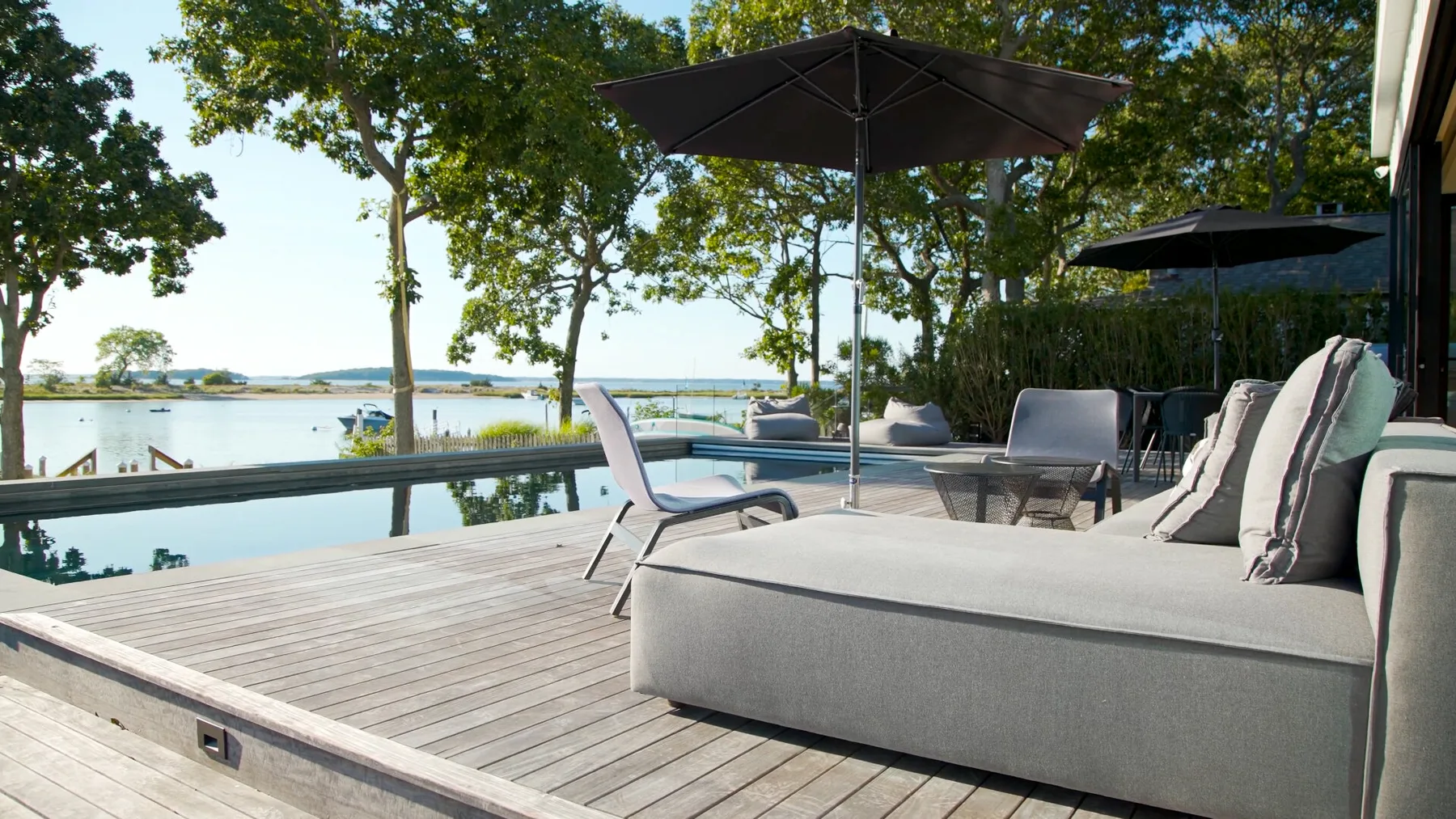 A waterside patio with outdoor seating and a large umbrella overlooks the water.