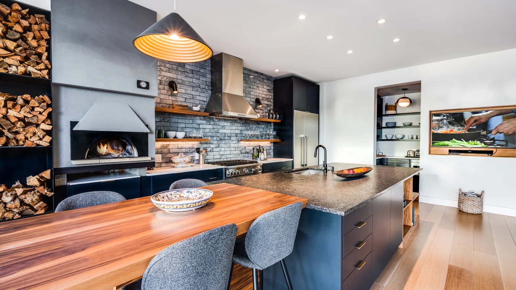 A modern kitchen with a central island, dining table, and wood-burning fireplace.