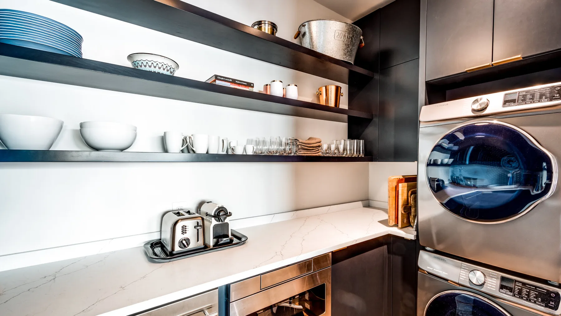 A modern kitchen counter with open shelves and a front-loading appliance.