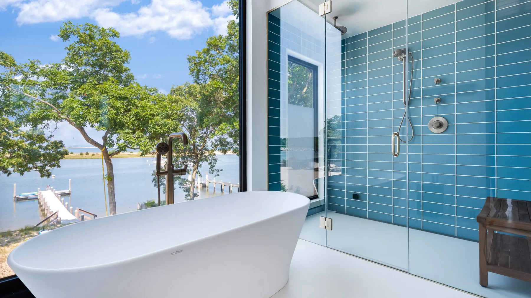 A bathroom with a freestanding bathtub beside a glass shower and blue tiled walls.