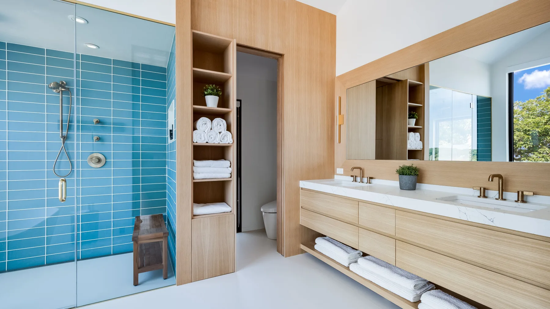 A modern bathroom with blue tiled walls, a shower, and a long vanity.