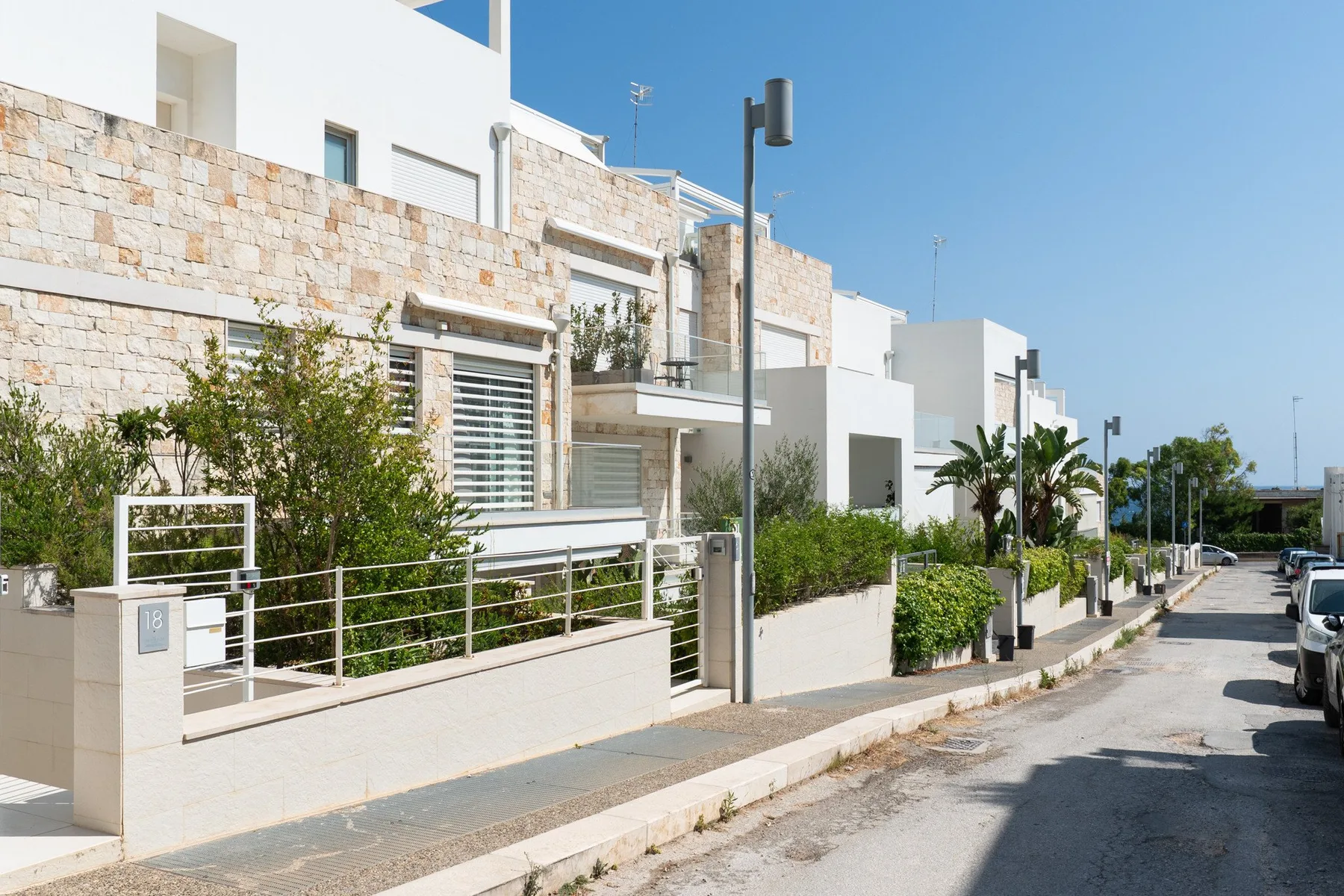 Una fila de casas modernas bordea una calle soleada con vegetación junto a las aceras.