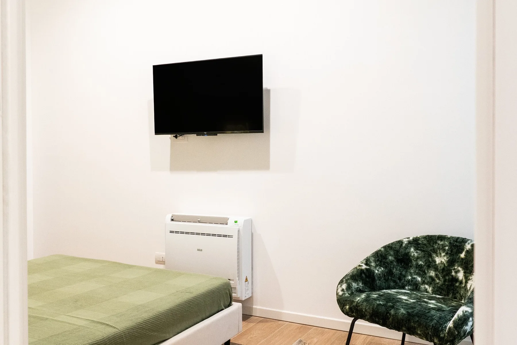 Un dormitorio con una cama, un televisor en la pared y asientos tapizados.